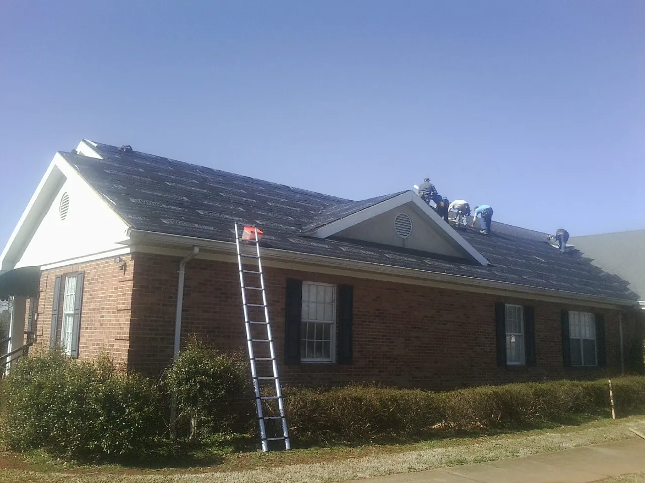 Crew tearing shingles off a brick ranch roof with a ladder set — Metal Roof Repair work by our crew in Allendale